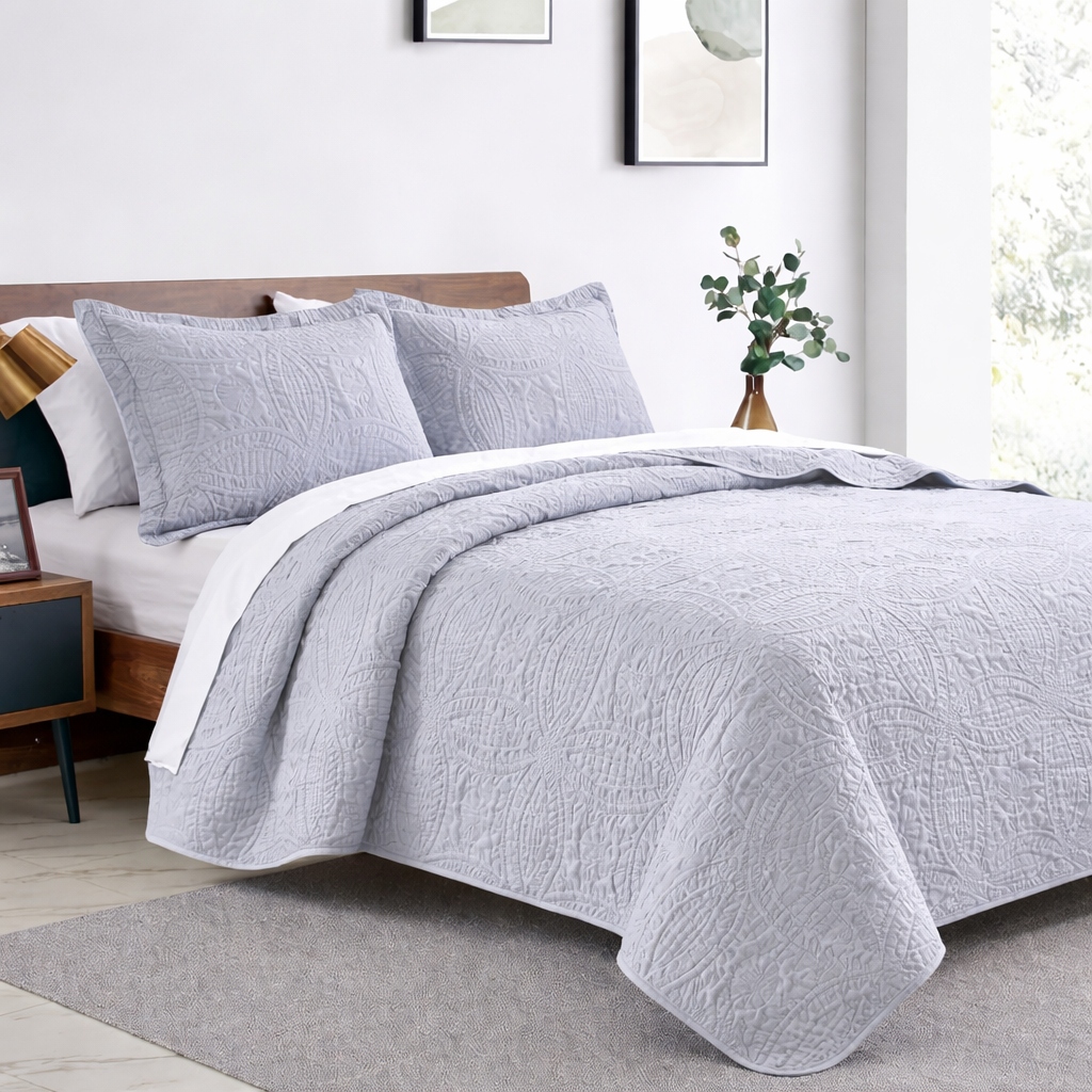 Decorative light grey quilted bedspread with matching pillow shams styled on a modern bed in an elegant bedroom interior