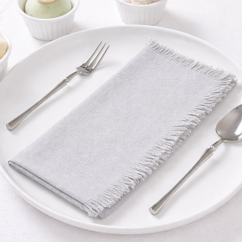 Soft light grey fabric napkin with fringe edges styled on a modern dining plate