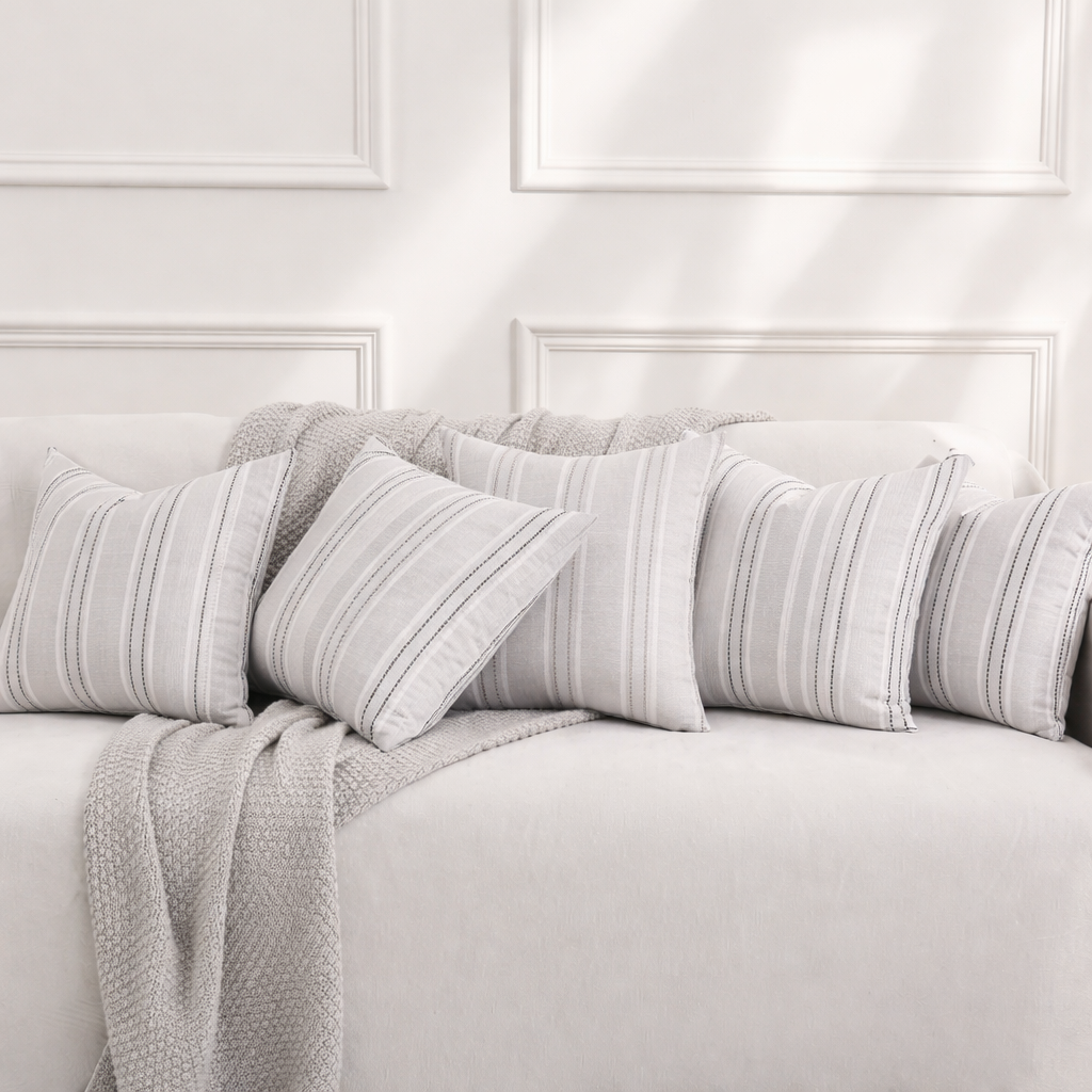 Stylish light grey striped pillow covers arranged on a luxury sofa with a soft knitted throw in an elegant modern interior